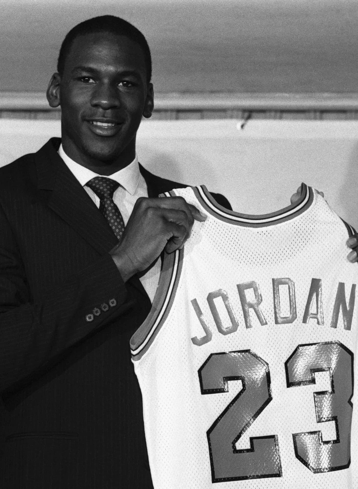 Michael Jordan in a suit holding up his number 23 Chicago Bulls jersey.